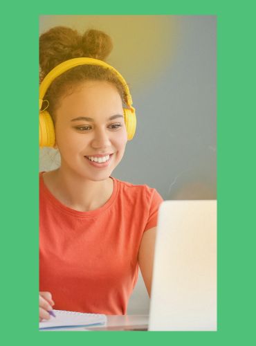 A woman wearing yellow headphones is smiling and looking at a laptop screen.