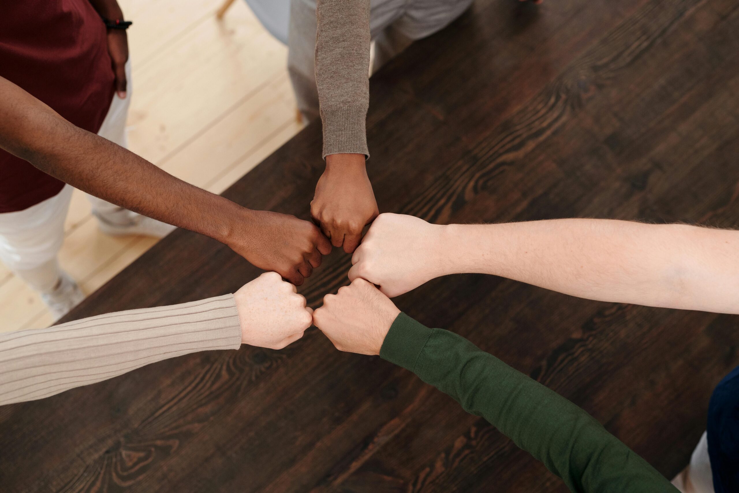 Top view of diverse hands fist bumping on wooden table, symbolizing teamwork, unity, and cooperation. Neurodivergent adults.